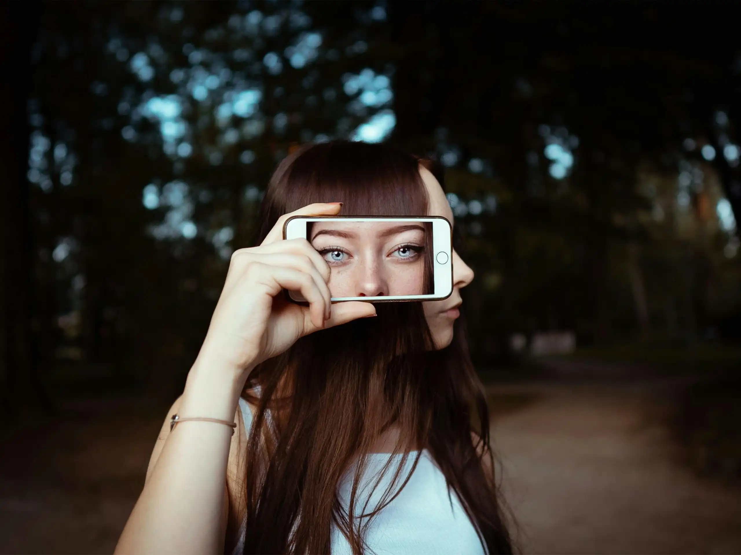 Profil d'une femme masquant son regard avec un téléphone montrant une photo de face de ses yeux.